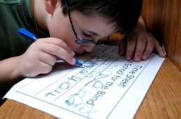 Boy wearing glasses writes on his time sheet with a thick blue marker.